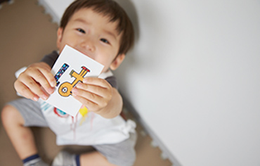 おがた歯科の特徴ー小児カウンセリング・託児システムのイメージ画像。子どもが ”は”という文字が書かれたカードをこちらに見せて遊んでいる